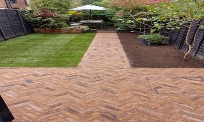 Sunny back garden patio with vibrant yellow brick paving and fresh turf in London 