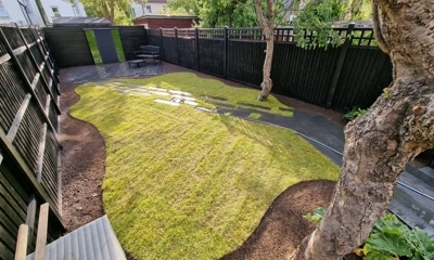 Artistic turf waves encircle granite stepping stone planks in vibrant landscaping.