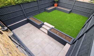 Artificial lawn, deep blue planter, and painted fence create inviting backyard.