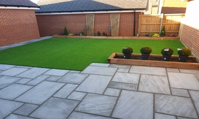 French pattern gray sandstone patio, wood planters beside vibrant artificial lawn.