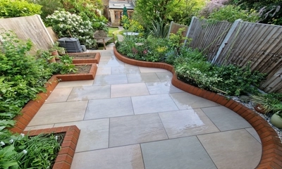 Raj Green porcelain paving embraced by red brick planters, harmonious elegance.