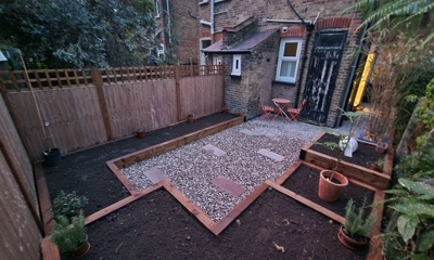 Varied wooden planters surround a pebble walkway, crafted from rustic sleepers.