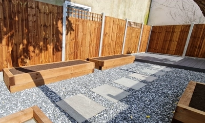 Wood sleeper planters surrounded by black ice stones, creating elegant contrast.